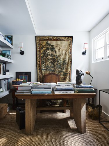 white maximalist home office with earthy accents, a wooden desk and tapestry hanging behind the desk