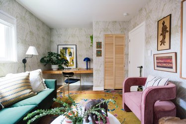 subdued maximalist home office with leafy wallpaper, pink sofa, green sofa and plants