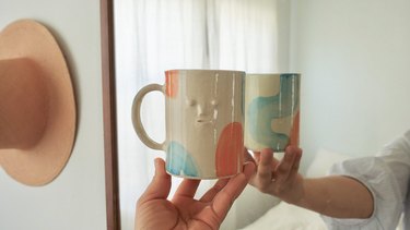 person holding mug with face and colors up to mirror