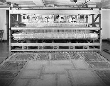 figures at a large loom with a rug in front of them