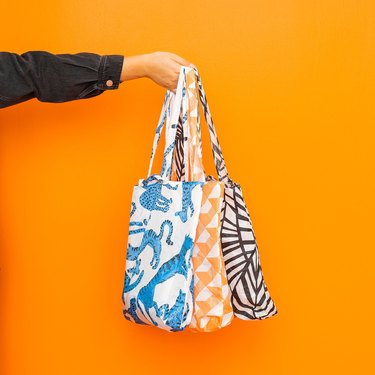 person holding shopping bags in various colors against an orange background