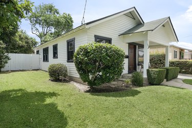 White craftsman house with a green lawn; shapely shrubs are planted in front of the porch and along the side