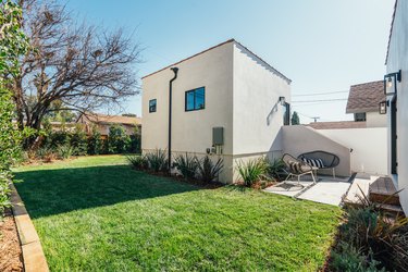 The backyard of a white stucco house with a lush green lawn