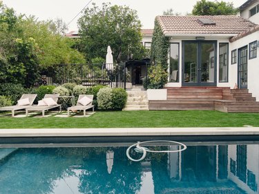 A white house with steps leading down to the backyard; an in-ground pool surrounded by a green lawn