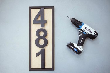 Modern black house numbers attached to wood board with power drill