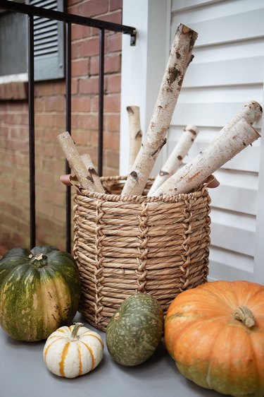 Birch logs stored inside basket with leather handles with pumpkins on floor around it