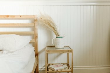 Dried grasses in a white pitcher on nightstand by bed