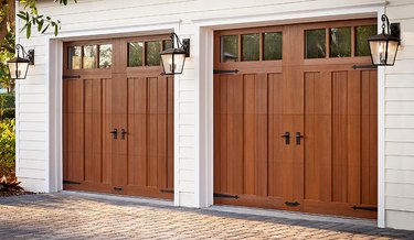 pair of wooden garage doors with paneling and windows flanked by wall sconces