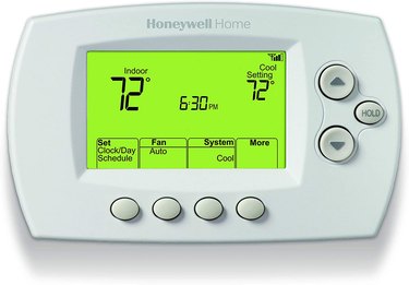 White rounded rectangular thermostat with green backlit interface