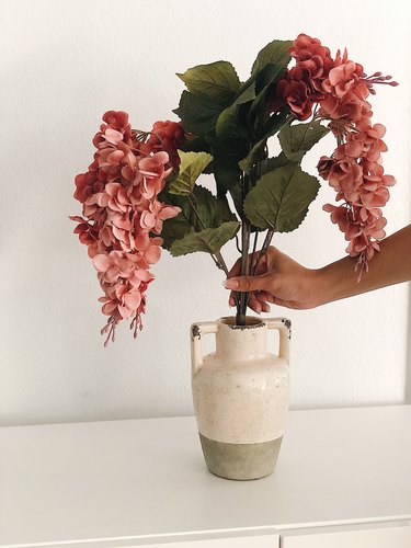 Adding faux flowers to a rustic vase.