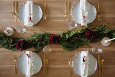 Holiday dinner table setting with pine garland and berry toned flowers and berries