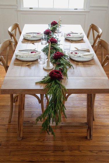 Holiday dinner table setting with pine garland and berry toned flowers and berries