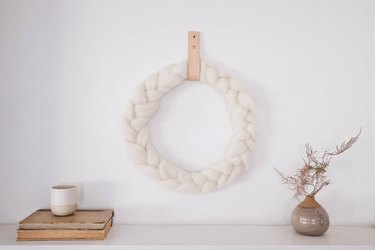 DIY braided ivory wool wreath hung on wall with leather strap