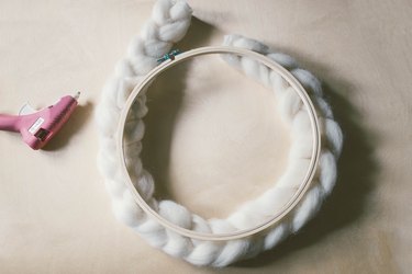 Hot gluing braided wool around wood embroidery hoop