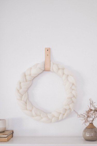 DIY braided ivory wool wreath hung on wall with leather strap