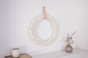 DIY braided ivory wool wreath hung on wall with leather strap