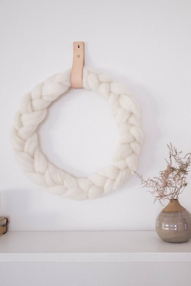 DIY braided ivory wool wreath hung on wall with leather strap