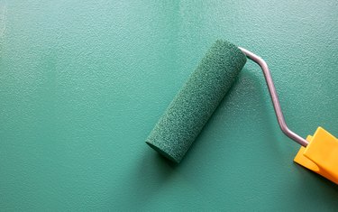 Paint roller with green or teal color on painted wooden surface.
