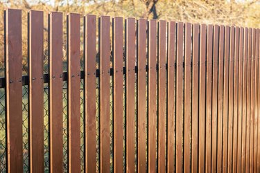 New modern brown wooden fence on chain-link fence.