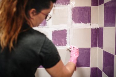 Young woman painting her bathroom tiles white