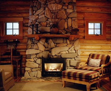 Armchair beside stone fireplace in log cabin.