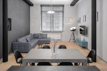 Small living room with dining table, miniblinds on window, gray sectional sofa.