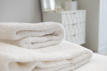 Two white fluffy towels folded on a white bed