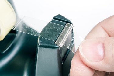 Macro of a hand pulling some tape off a black dispenser.