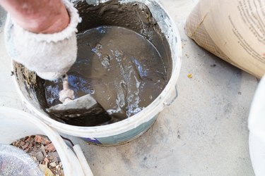 a gloved man's hand kneads cement mortar with a trowel.