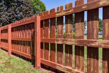 Wooden privacy fence in backyard with pickets being painted red