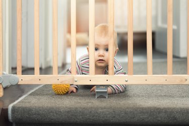 baby playing with ball behind safety gates