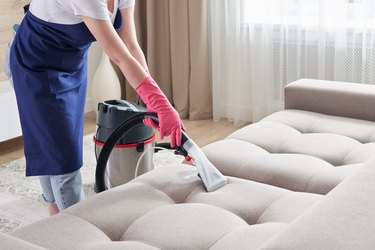 Woman cleaning couch with vacuum cleaner at home. Cleaning service concept