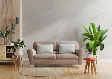 Brown sofa and a wooden table in living room interior with plant, concrete wall.