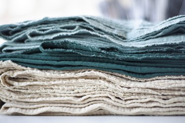Cotton textiles in shades of green and beige in a stack. Organic cotton for the textile industry. Towels plaids sheets muslin clothes.
