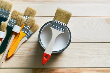 A Clean Brush On A Can Of White Paint. There Are A Lot Of Different Brushes Next To It, On A Wooden Background. Painting And Repair Work. The concept of the construction industry, professional and home repair.