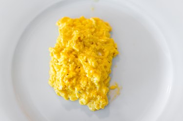 Flat top lay macro closeup of fresh egg scrambled eggs omelette in classic French cooking style on white plate cooked traditional morning breakfast with small creamy pieces texture and black pepper