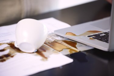 Closeup shot of coffee spilled over paperwork and a laptop on a table.
