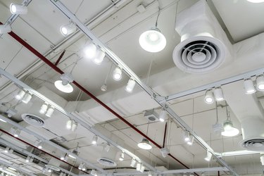 Bare ceiling with air duct, CCTV, air conditioner pipe and fire sprinkler system on white ceiling wall. Air flow and ventilation system. Ceiling lamp light with opened light. Interior architecture.