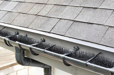 Plastic guard brush in new dark grey plastic rain gutter on asphalt shingles roof.