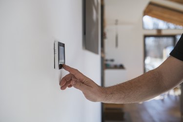 Man at home adjusting thermostat with device on the wall.