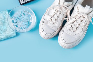 Dirty white sneakers with special tool for cleaning them on blue.
