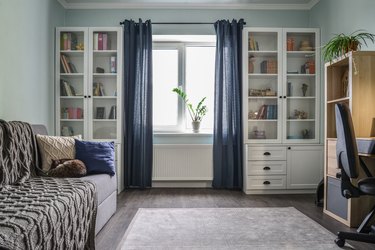 Light, cozy teen room with blue curtains, white shelving/drawers, beige area rug