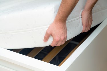 Man hands lifting the mattress at the bedroom. Looking at the bed frame, inspects the mattress