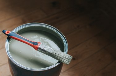 A small paintbrush sits on top of a large tin of light green / grey paint