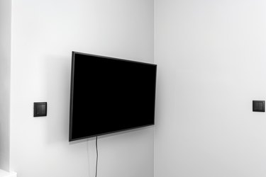 The TV is hung on the gray wall in the bedroom, the buttons for the blinds are visible.