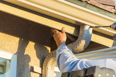 Worker Attaching Aluminum Rain Gutter to Fascia of House.