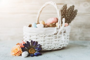 White easter wicker basket with multicolored flowers and eggs.