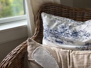 rattan wicker chair with throw pillows beside window with view of marsh