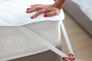 Woman puts blanket or mattress topper on bed closeup