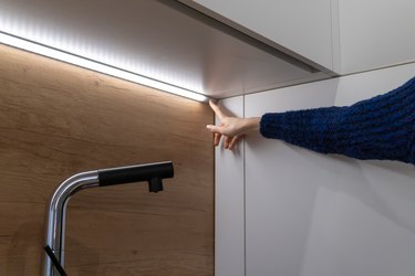 Female hand includes an LED strip for lighting on the cabinet surface on the kitchen set